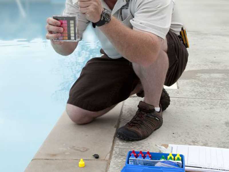 Testing pool water chlorine and pH levels with a test kit at the edge of a pool